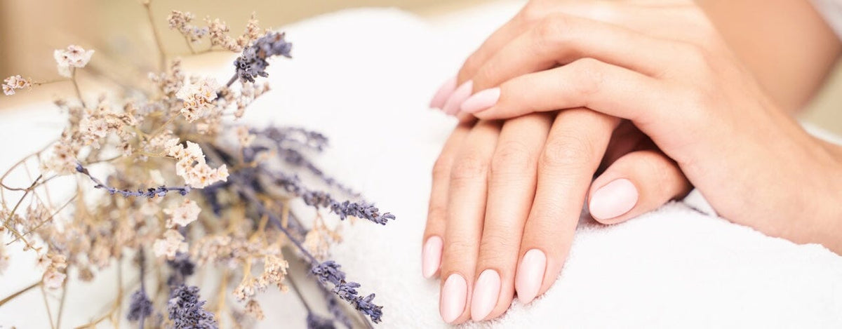 Hands with soft pink almond nails resting on a white towel beside dried lavender