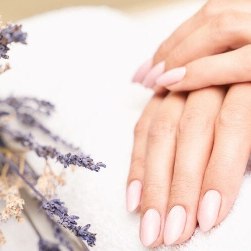 Hands with soft pink almond nails resting on a white towel beside dried lavender