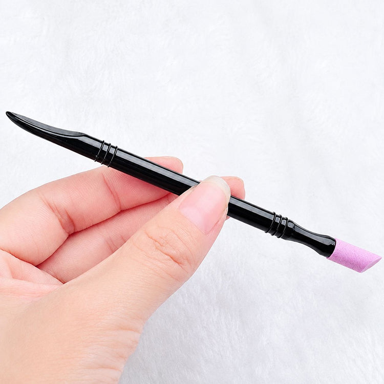 Hand holding 2-way stone cuticle remover and nail pusher tool with pink angled ceramic tip and black handle for manicure prep