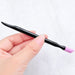 Hand holding 2-way stone cuticle remover and nail pusher tool with pink angled ceramic tip and black handle for manicure prep