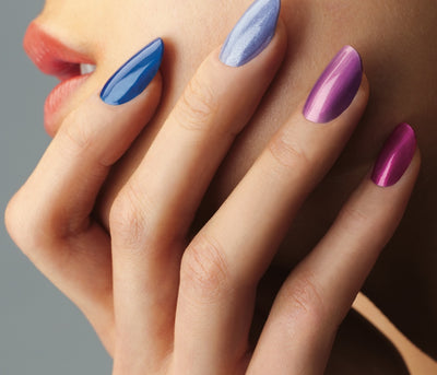 Close-up of a hand on a cheek with glossy almond-shaped nails in blue, lavender, purple, and magenta