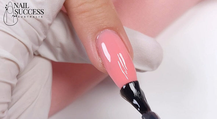 Gloved nail tech applying clear top coat to a pink BIAB builder-gel nail for a high-gloss finish