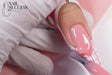 Gloved nail tech brushing pink HEMA-free BIAB builder gel onto a nail form to sculpt a salon-grade extension