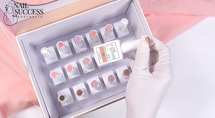Gloved hand holds Nail Success HEMA-Free Builder Gel (BIAB) bottle above boxed collection of pink and nude shades