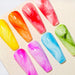 NSI Blooming Gel nail art swatches — eight glossy coffin tips with watercolor marble effects in yellow, orange, red, pink, blue and green on a neutral board