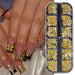 Assorted gold nail art charms set in clear organizer case, shown with nude and black rhinestone nails and gold bow charm