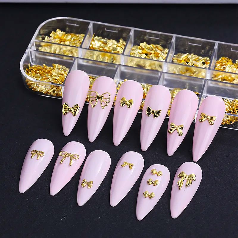 Gold bow nail art charms in organizer tray on pink stiletto nail tips, 3D metal bow decorations