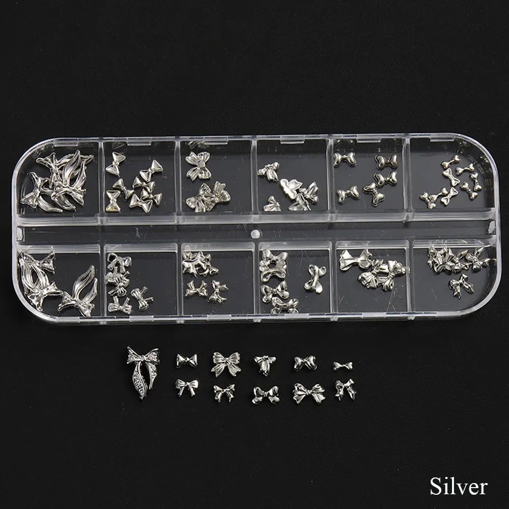 Silver 3D bow nail art charms set in clear compartment storage tray, assorted metal nail decorations on black background