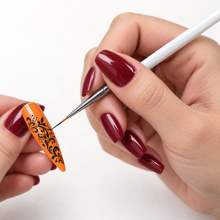 White-handled nail art liner brush painting intricate black floral scrollwork on a glossy orange stiletto nail tip.