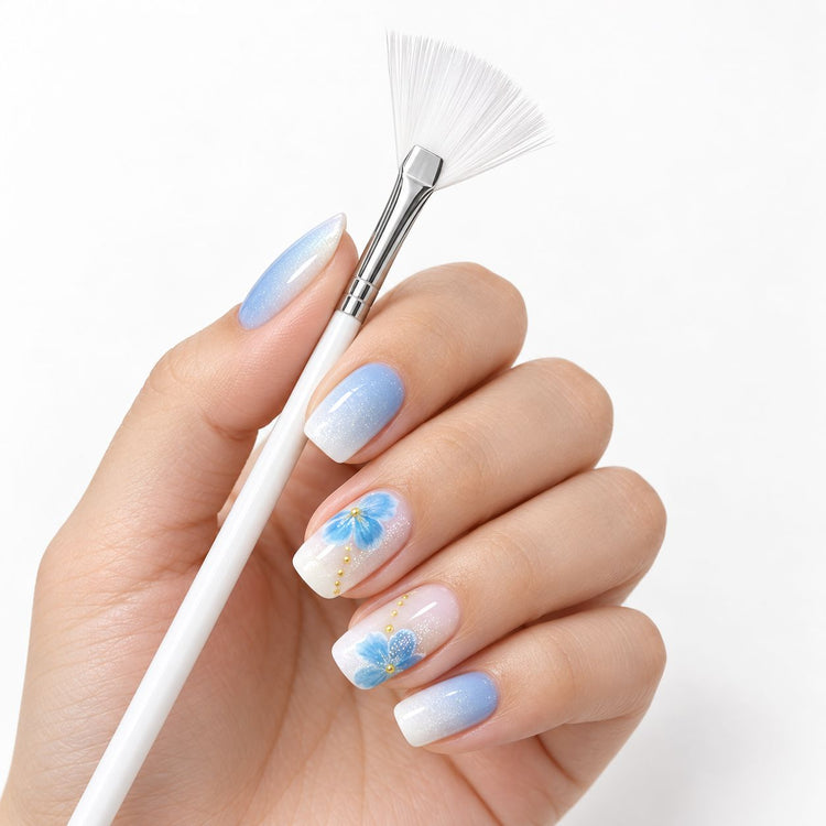 White fan brush held beside a blue and white floral gel manicure painted with the nail art brush set