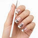 Nail art liner brush held beside a hand with fine black line work and rhinestone accent nails