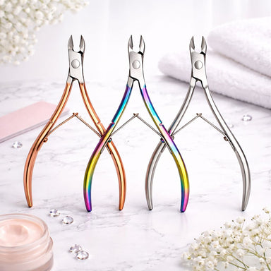 Three cuticle nippers in rose gold, rainbow and silver finishes displayed on a manicure table with towel, flowers and cream jar