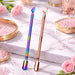 Rainbow and rose gold double-ended cuticle pushers and scrapers displayed on a marble beauty surface with pink roses and crystal accents