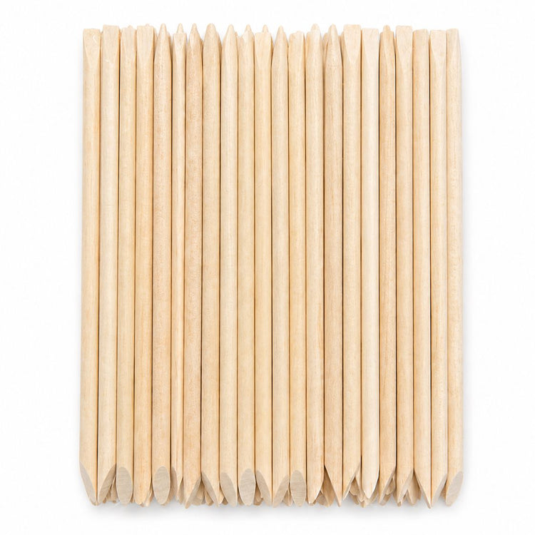 Bundle of wooden cuticle pusher sticks with pointed tips and large angled flat ends arranged on a white background