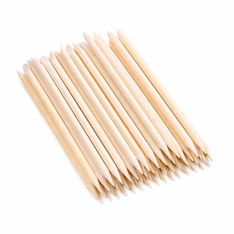 Wooden cuticle pusher sticks stacked diagonally, showing pointed tips and angled flat ends on a light gray background