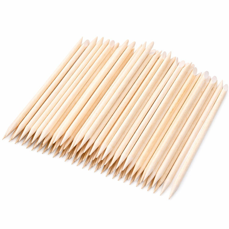 Wooden cuticle pusher sticks arranged in a fan shape, showing pointed tips and angled flat ends on a light gray background