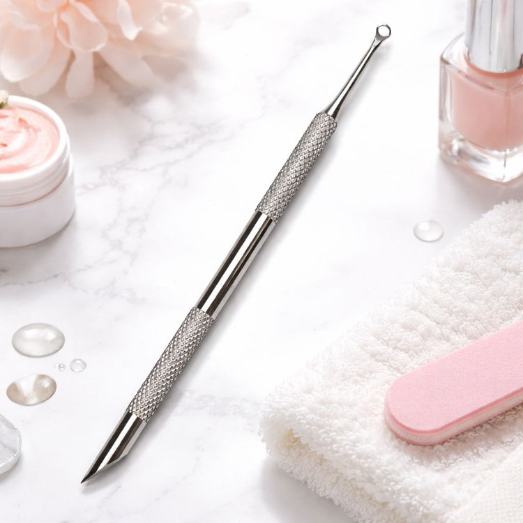 Stainless steel cuticle scraper and pusher with loop-detail tip and angled precision scraper, displayed on a manicure setup with nail polish, towel and nail file