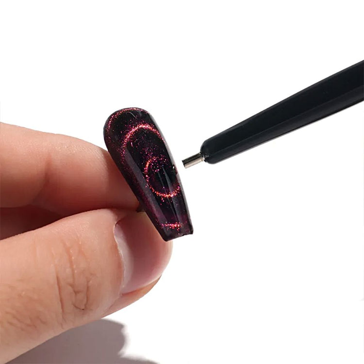 Black double-ended magnetic nail art stick creating pink cat eye gel polish swirl effects on a false nail tip for magnetic nail designs