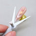 Scissor-shaped double-ended cat eye magnet tool creating cat-eye highlight on pink magnetic gel nail tip