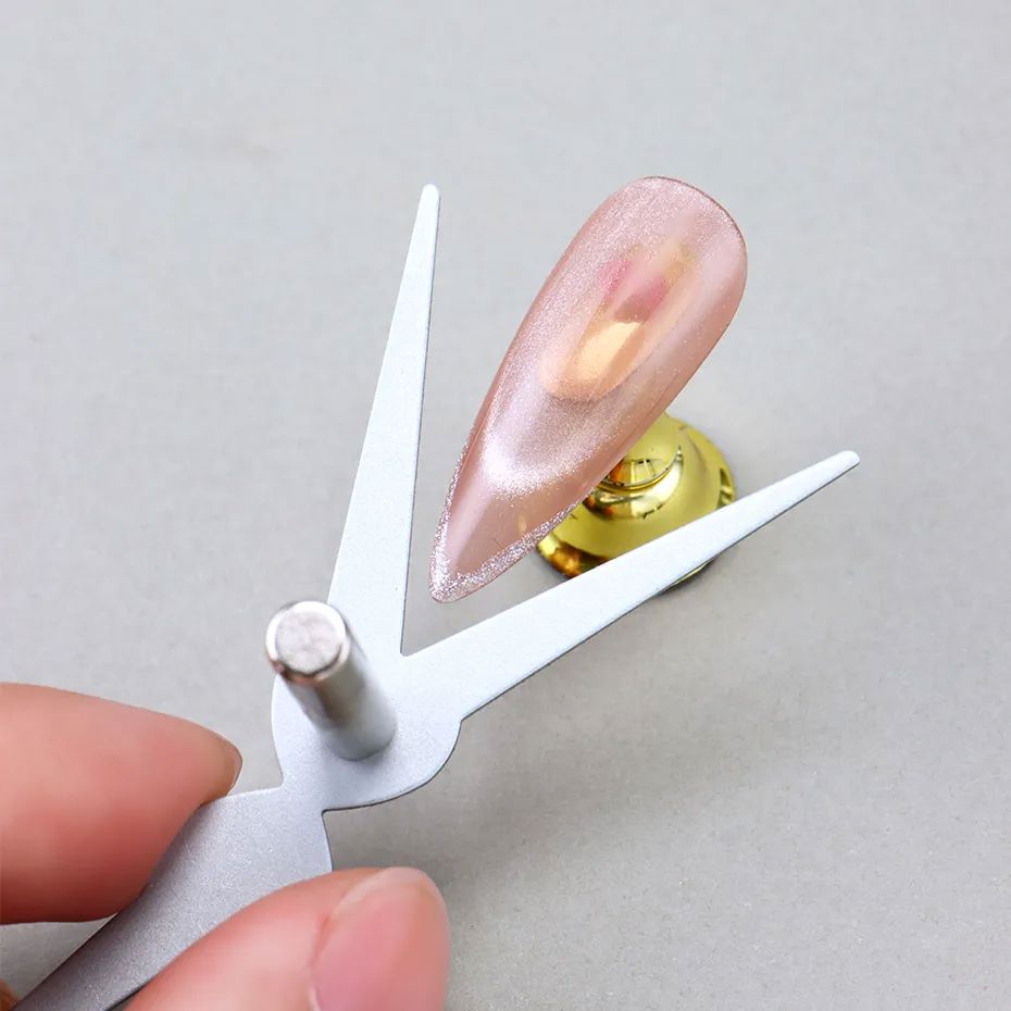 Scissor-shaped double-ended cat eye magnet tool creating cat-eye highlight on pink magnetic gel nail tip
