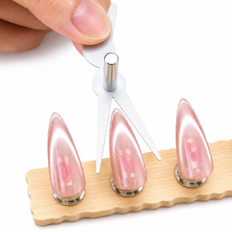 Silver scissor-shaped cat-eye magnet tool being used over three pink cat-eye stiletto swatch nails on a wooden holder