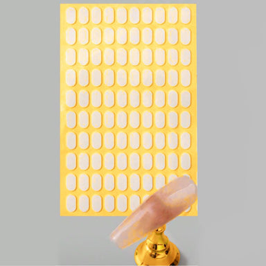 Double-sided adhesive tabs sheet for nail tip display stands, with clear practice nail tip on gold holder for nail art swatches