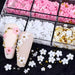 White & pink 3D flower nail art charms — mixed-size daisies with pearls and gold beads in organizer, shown on nude nail tips