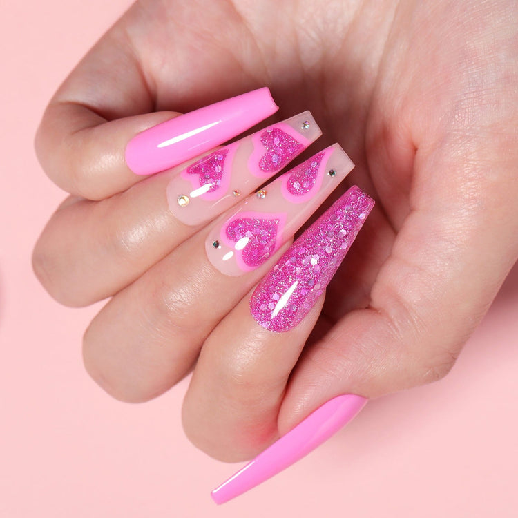 Hot pink gel polish with glitter hearts and rhinestones on long coffin nails over a glossy nude base