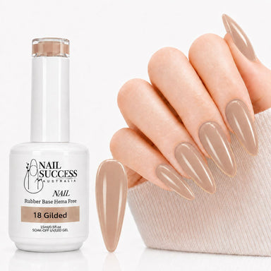 A bottle of Nail Success Australia 18 Gilded nude gel nail polish next to a hand with long, glossy, almond-shaped nails in the matching nude shade - HEMA Free Rubber Base Gel.