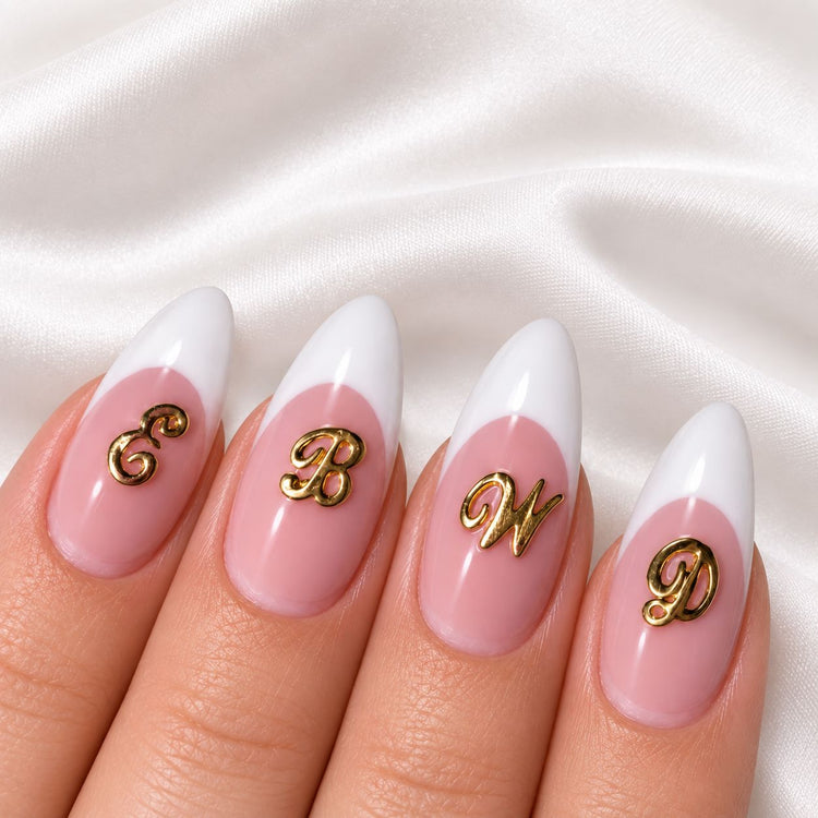 Gold script letter nail art charms on pink and white French tip almond nails