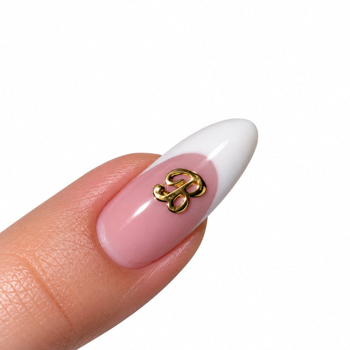 Gold script letter B nail art charm on a pink French tip almond nail