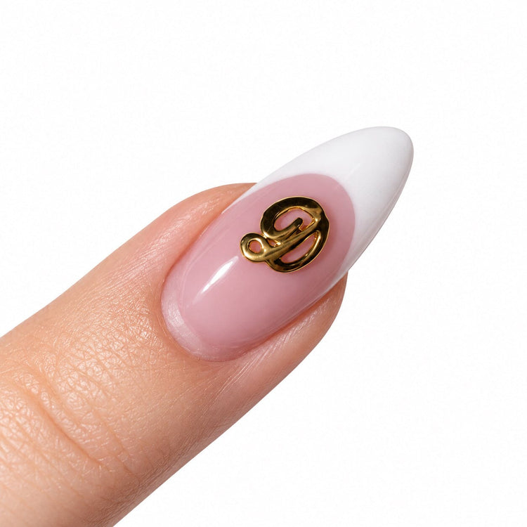 Gold script letter D nail art charm on a pink French tip almond nail