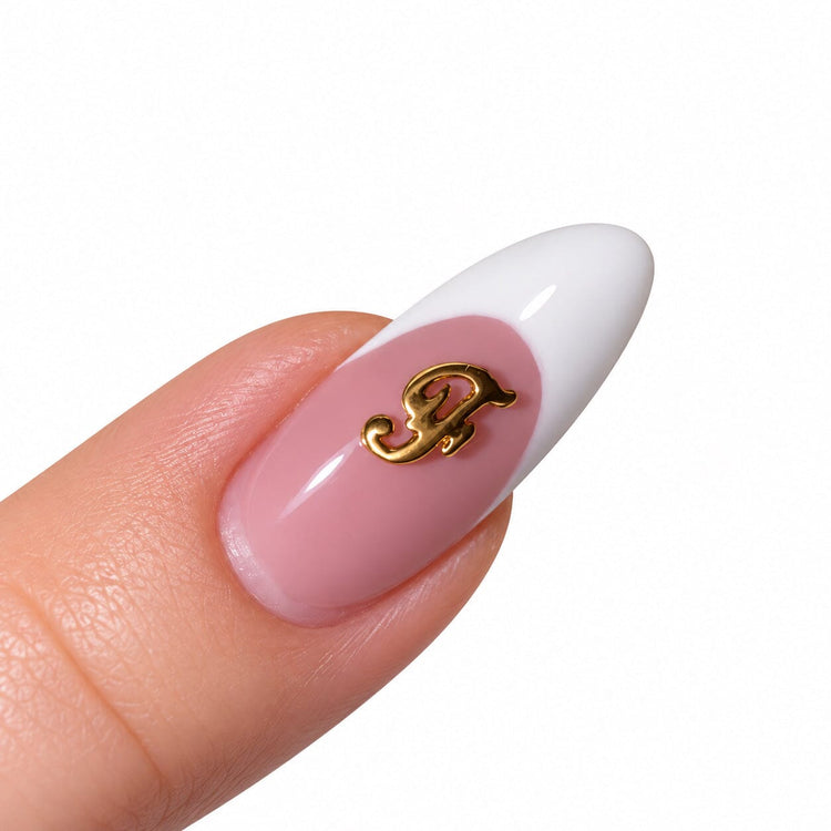 Gold script letter F nail art charm on a pink French tip almond nail
