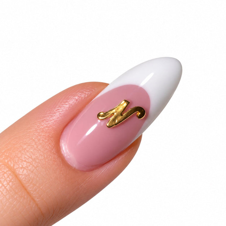 Gold script letter N nail art charm on a pink French tip almond nail