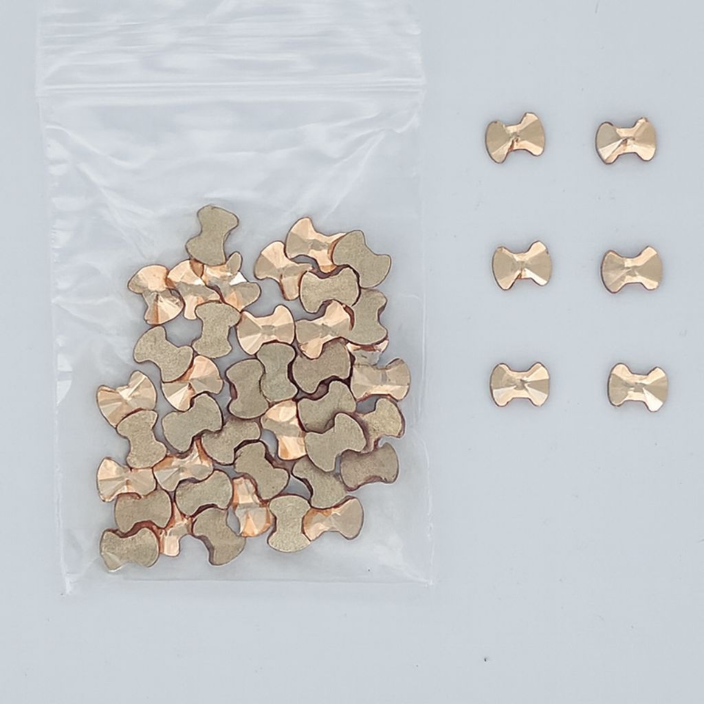 Gold bow-shaped nail art rhinestones — faceted flatbacks in zip bag with loose samples (NSI Australia)