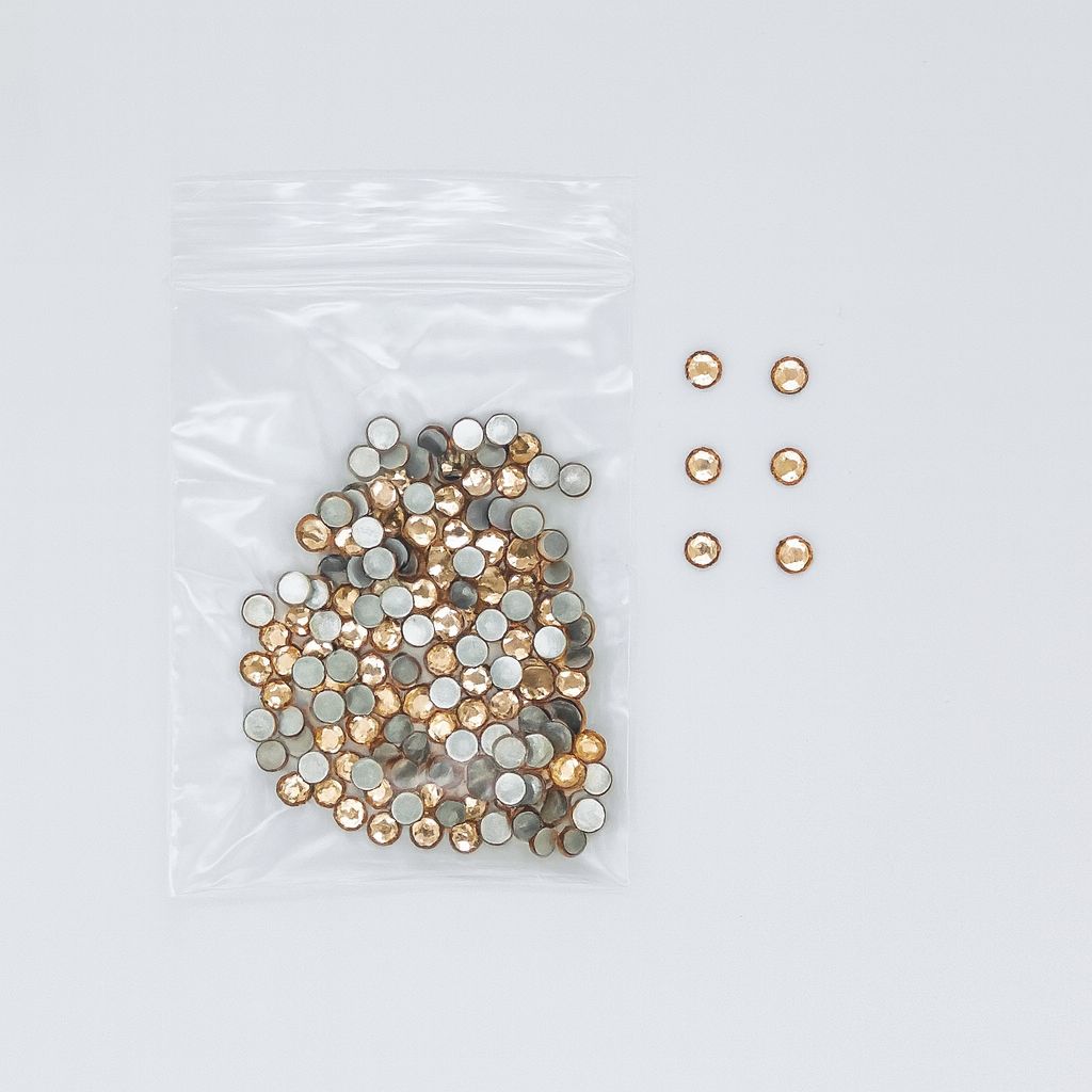 Pack of round champagne-gold flat‑back nail rhinestones (2.7 mm) in a clear zip bag, with a few shown; NSI Australia