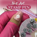 Nail art stamp pen with metal pattern tips, pressing a white flower design onto a pink nail
