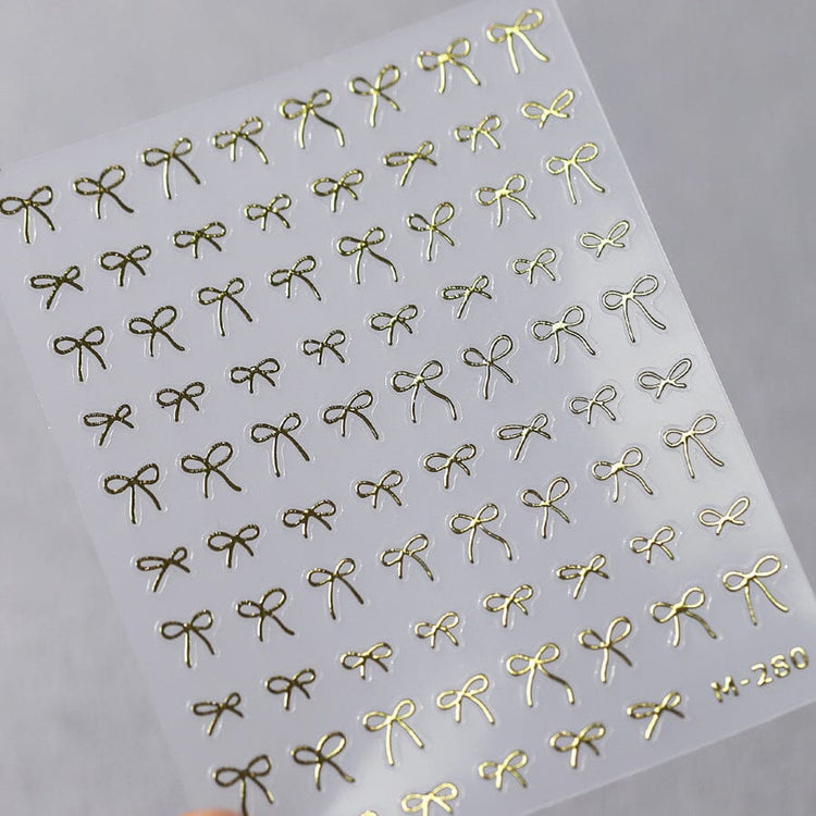 Gold bow nail art stickers sheet with delicate metallic ribbon designs for elegant salon manicure decorations