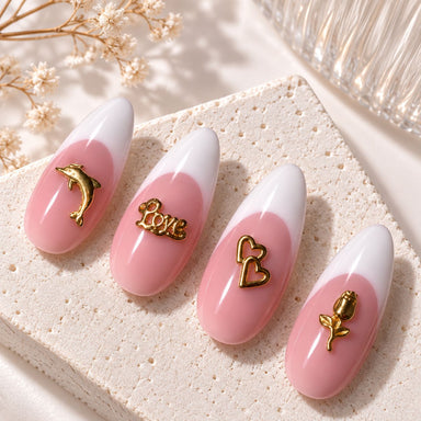 Gold dolphin, “Love”, double-heart and rose nail charms displayed on pink and white French almond nail tips.