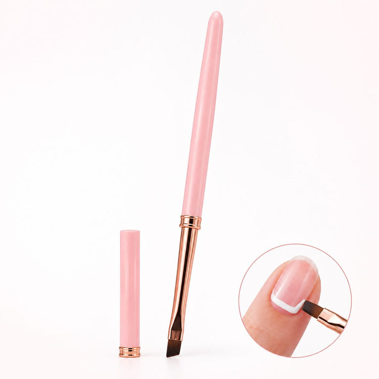 Pink angled gel nail brush with rose gold ferrule and matching cap, shown painting a white outline on a natural nail.
