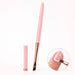 Pink angled gel nail brush with rose gold ferrule and matching cap, shown painting a white outline on a natural nail.
