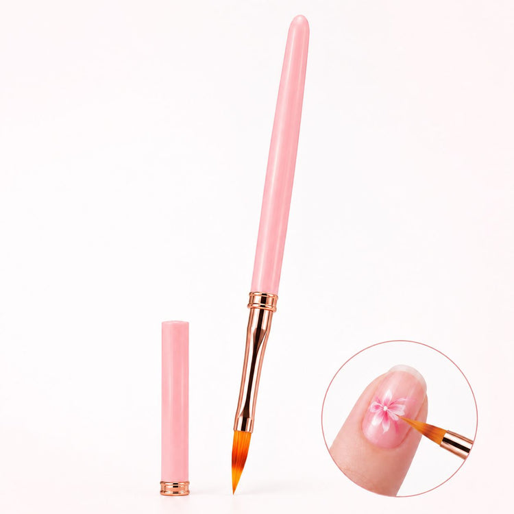 Pink pointed nail art brush with rose gold ferrule and matching cap, shown painting a pink and white flower on a natural nail.
