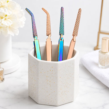 Rainbow and rose gold multi-function nail tweezers with textured grip displayed in a ceramic salon tool holder