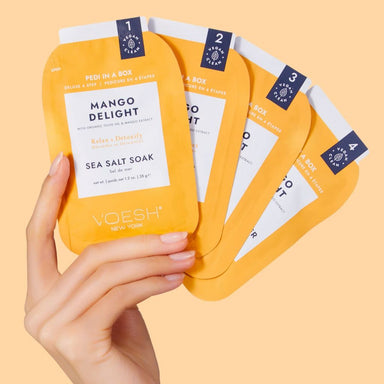 Hand holding VOESH New York Pedi in a Box Mango Delight deluxe 4-step pedicure kit sachets