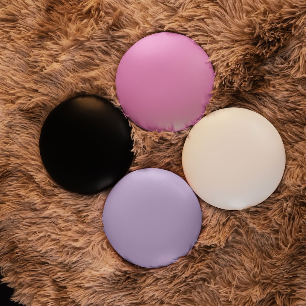 NSI Pro Elbow Pad Pillow Rest – round manicure arm support cushions for nail techs in black, pink, lilac and ivory, shown on a plush rug