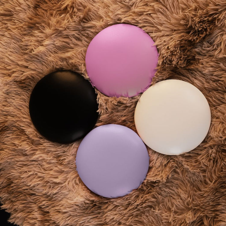 NSI Pro Elbow Pad Pillow Rest – round manicure arm support cushions for nail techs in black, pink, lilac and ivory, shown on a plush rug