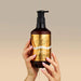 Hands holding Voesh 24K Gold vegan hand and body crème pump bottle, 829ml