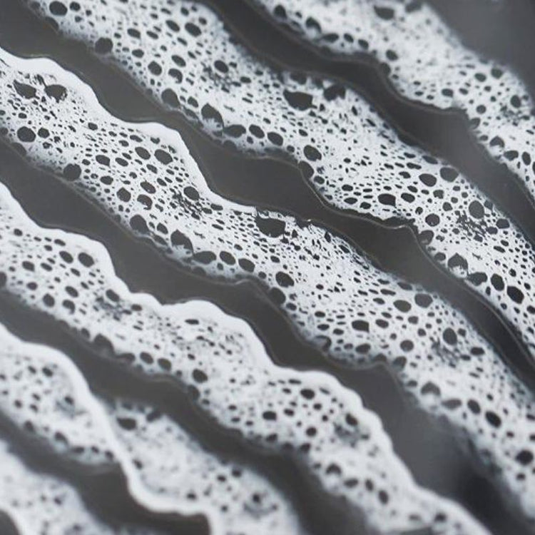 Close-up of 3D ocean wave nail art sticker with white sea foam pattern on grey background